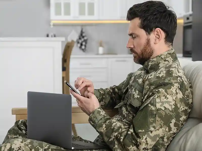 Military person in uniform using their laptop and phone on the couch